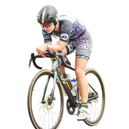 Abgebildet ist eine Person auf einem Rennrad. Die Person trägt einen Helm, eine Sonnenbrille und halblange, bunt gemusterte Radlerkleidung.