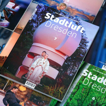 Abgebildet sind mehrere Ausgaben des „Stadtluft Dresden Magazins“. In der Mitte liegt leicht schräg die Ausgabe 7. Das Cover zeigt eine männliche und eine weibliche Person vor einer Art Sternwarte, die über eine Spindeltreppe erreichbar ist.
